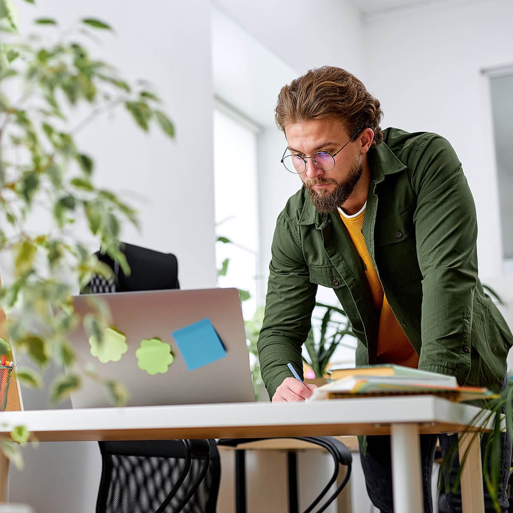 Man checking details on a laptop and making notes.